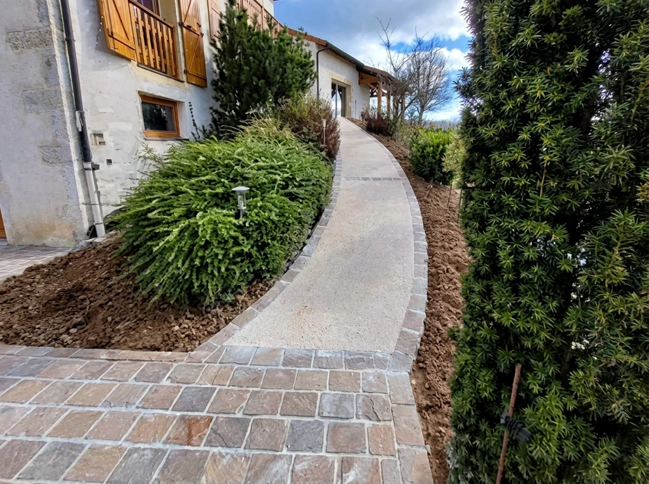 Allée courbe extérieure reliant une entrée de maison, bordée de cyprès et arbustes