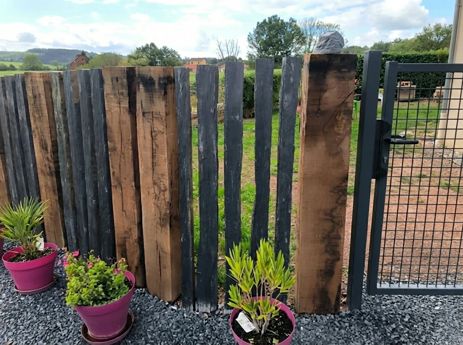 Clôture de jardin extérieure composée de madriers en bois massif recyclé, alternant planches naturelles brutes et planches noircies au brûlage (technique Shou Sugi Ban)