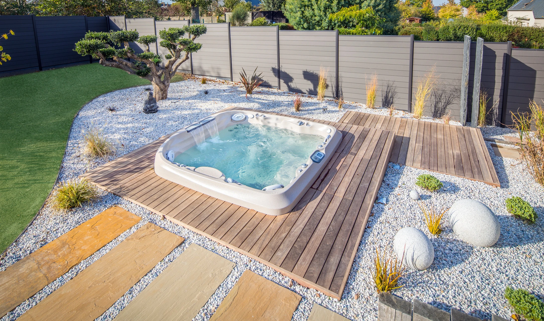 Aménagement extérieur contemporain avec spa encastré dans terrasse bois exotique, jardin zen minéral avec galets blancs, graminées ornementales et sphères décoratives